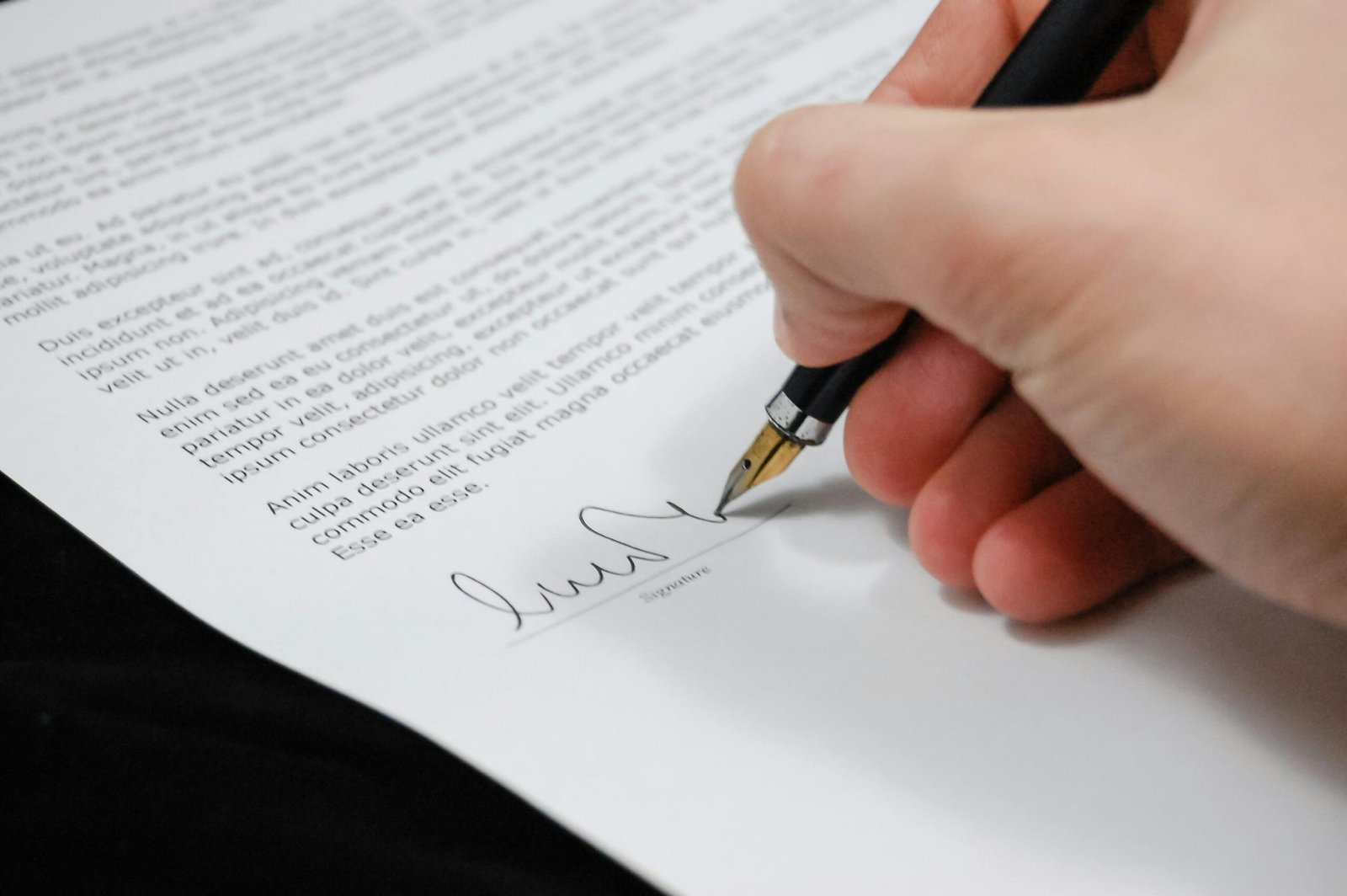 Services Close-up of a hand signing a legal document with a fountain pen, symbolizing signature and agreement.